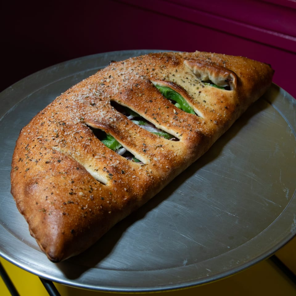 A golden-brown calzone, topped with herbs and salt, sits on a metal pizza pan.