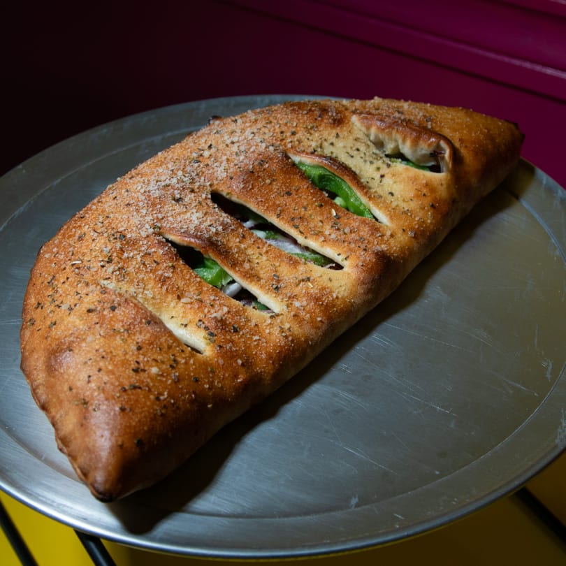 A golden-brown calzone, topped with herbs and salt, sits on a metal pizza pan.