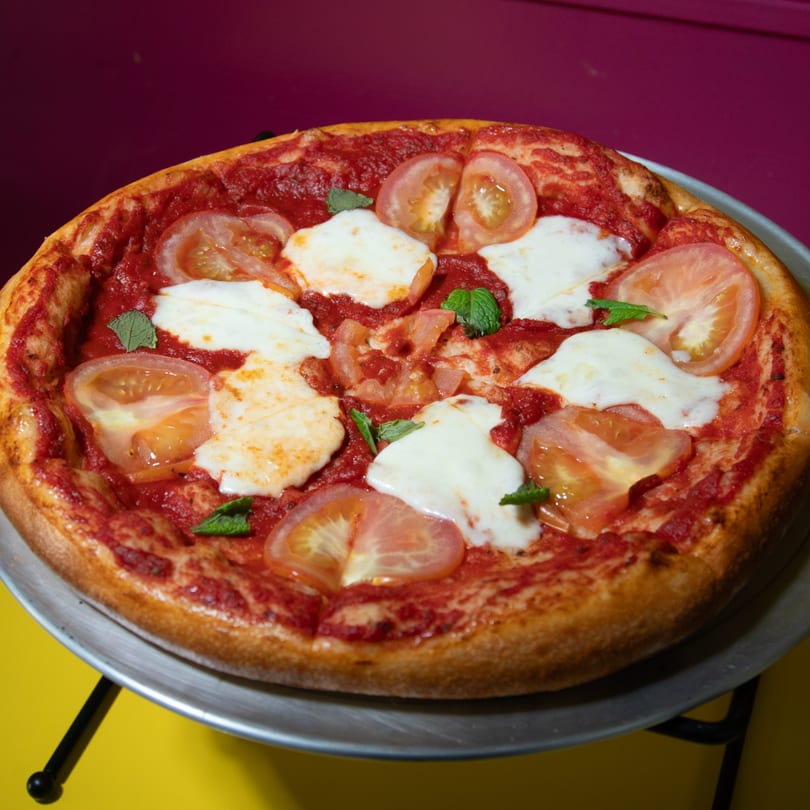 Margherita pizza with tomato sauce, fresh mozzarella, sliced tomatoes, and basil on a metal stand.